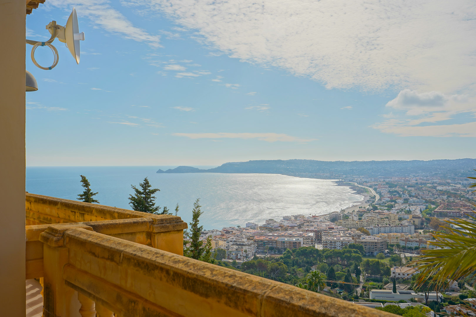 Panoramisch uitzicht vanaf het terras met stenen balustrade over de baai van Jávea, de haven en het silhouet van Cap Negre in de verte.
