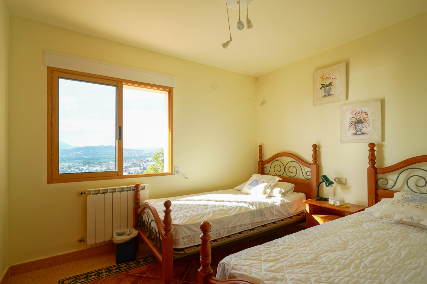 Slaapkamer met twee houten eenpersoonsbedden, tegelvloer en een groot raam met panoramisch uitzicht over de vallei en de bergen van Jávea.