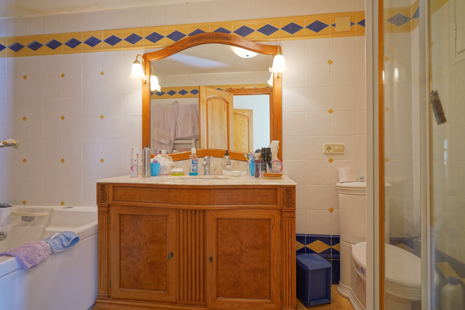 Traditionele badkamer met een bewerkt houten wastafelmeubel, marmeren blad en wandtegels met blauwe en gele decoratieve randen.