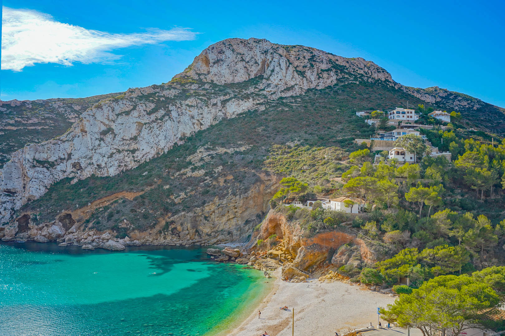 Panoramisch uitzicht op de baai van Granadella met turquoise water, kalkstenen kliffen en mediterrane begroeiing rondom het kiezelstrand.