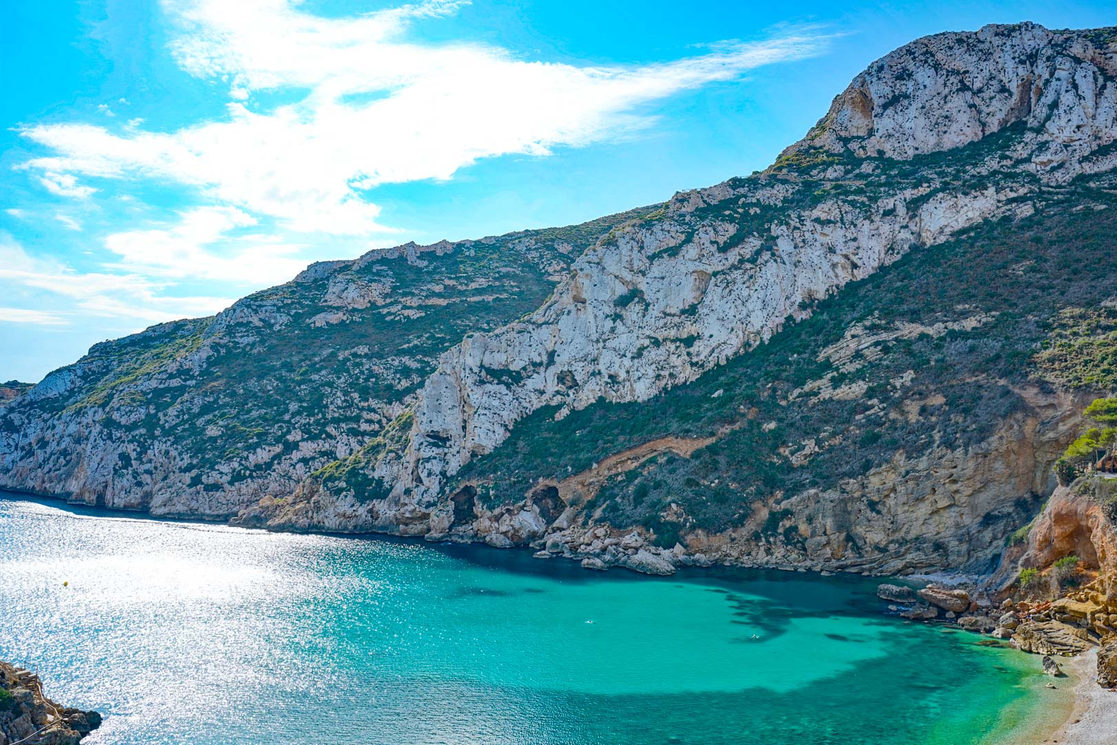 Panoramisch uitzicht op het turquoise water van de baai van Granadella, omgeven door steile kalkrotsen en mediterrane begroeiing.