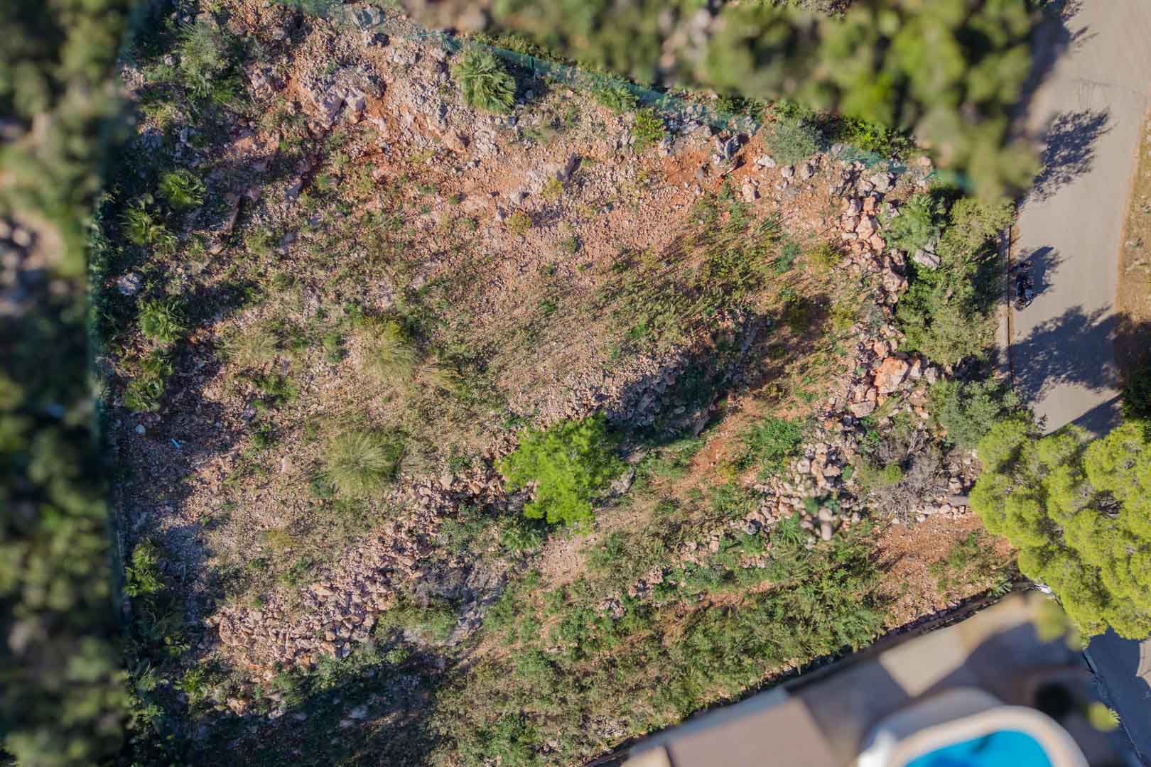 Bovenaanzicht van het omheinde perceel in Montepego, met natuurlijk rotsachtig terrein en directe toegang via de geasfalteerde weg.
