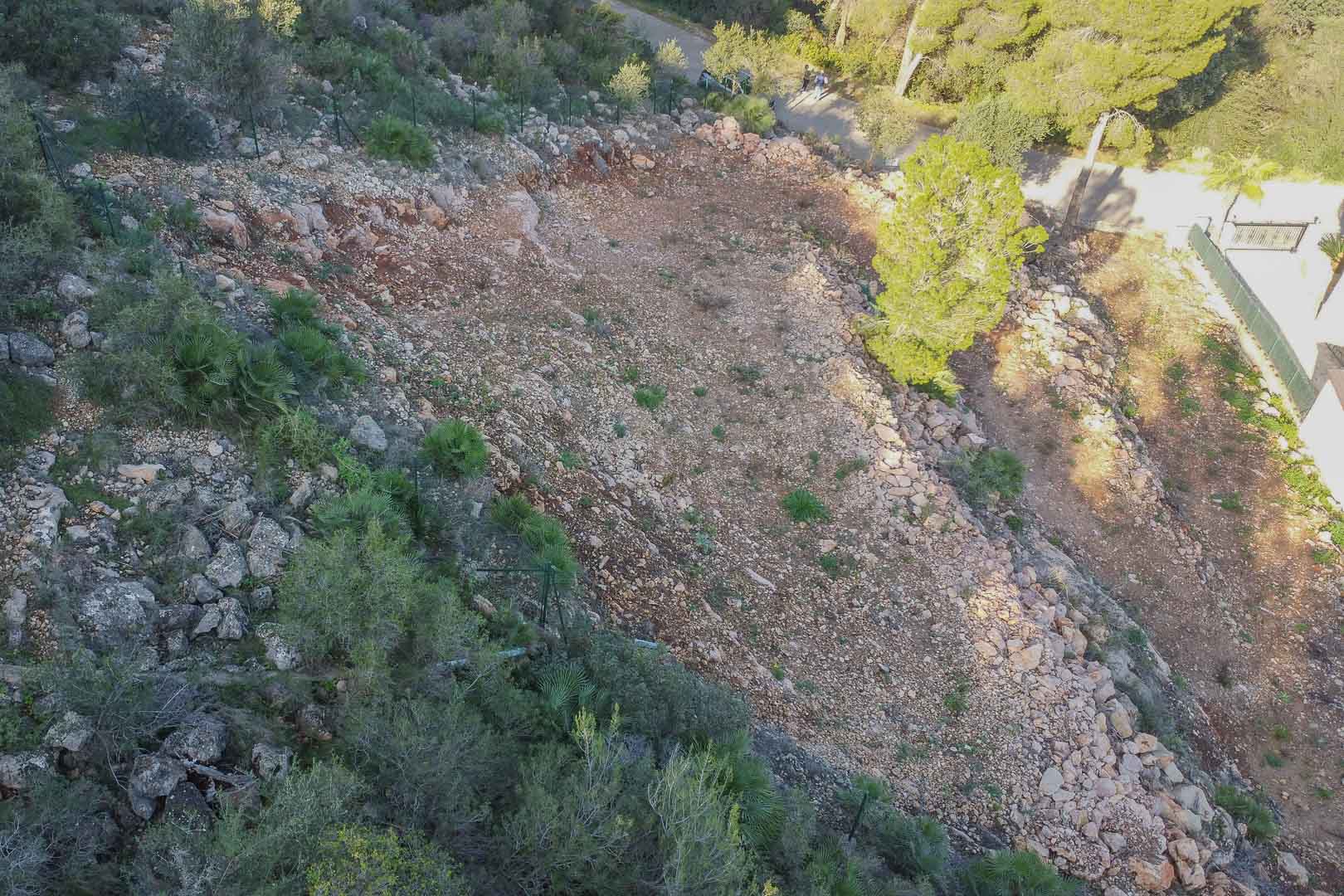 Geterrasseerd bouwperceel in Montepego met vrijgemaakte rotsachtige grond, omheining en mediterrane begroeiing, gelegen nabij de toegangsweg.