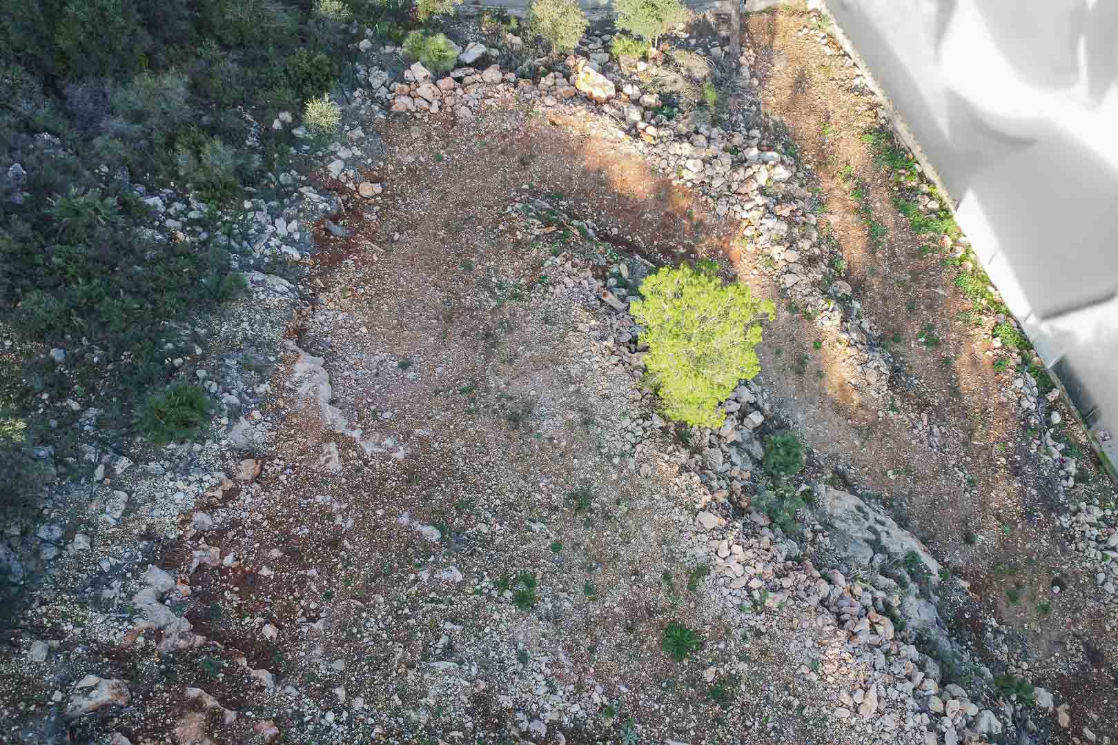 Luchtfoto van het bouwperceel met rotsachtige grond en inheemse struiken. Het terrein is bouwrijp gemaakt en voorzien van een duidelijke omheining.