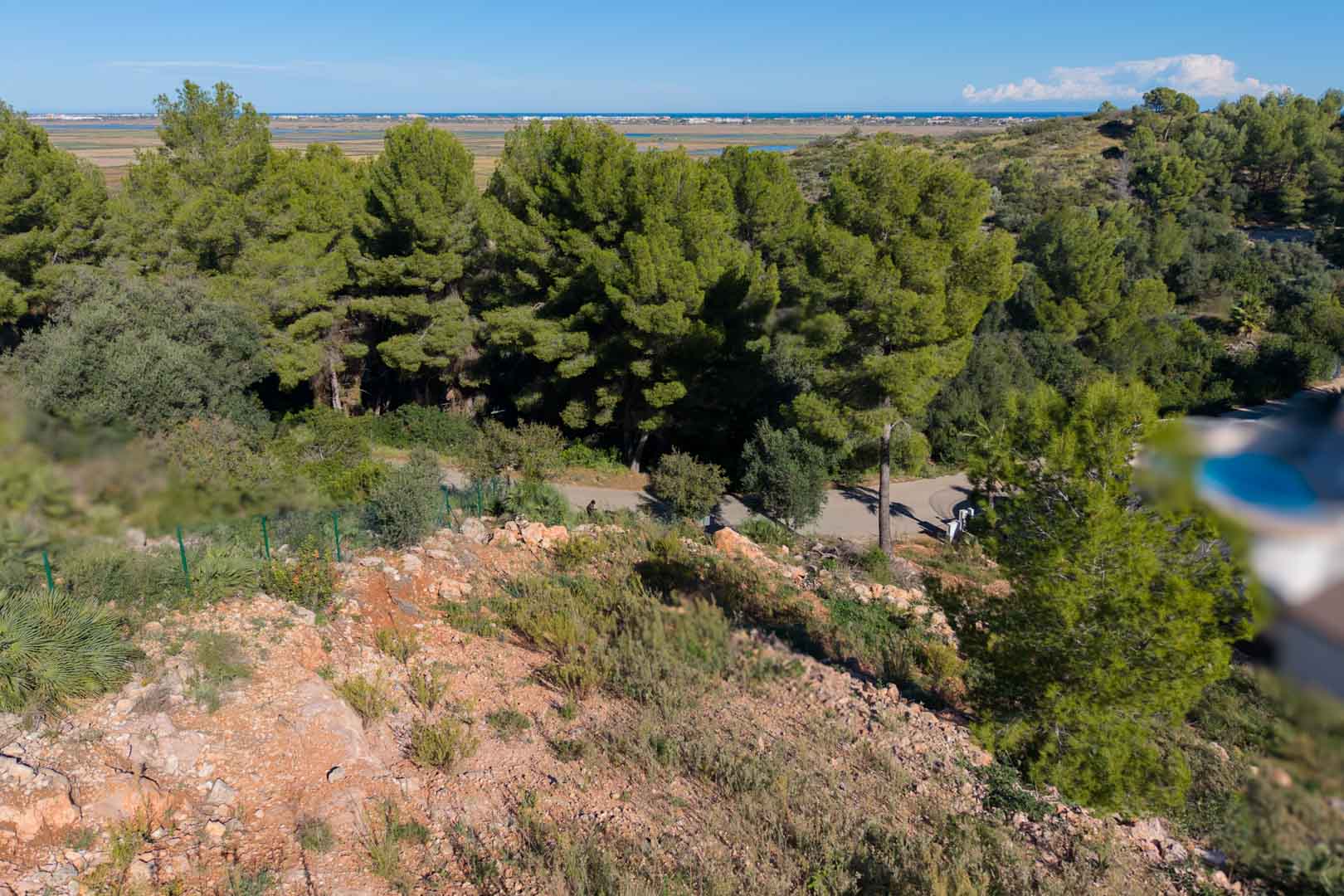 Panoramisch uitzicht vanaf het verhoogde perceel over het natuurpark Marjal de Pego en de Middellandse Zee, omgeven door pijnbomen en ruig terrein.
