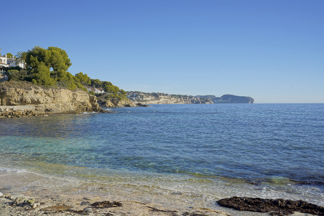 Uitzicht op een baai in Calpe met helder turquoise water, kalkstenen kliffen en mediterrane pijnbomen onder een strakblauwe lucht.