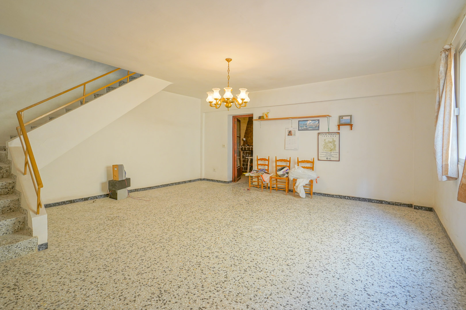 Centrale woonkamer met originele terrazzovloer, klassieke kroonluchter en trap met metalen leuning die naar de bovenverdieping leidt.