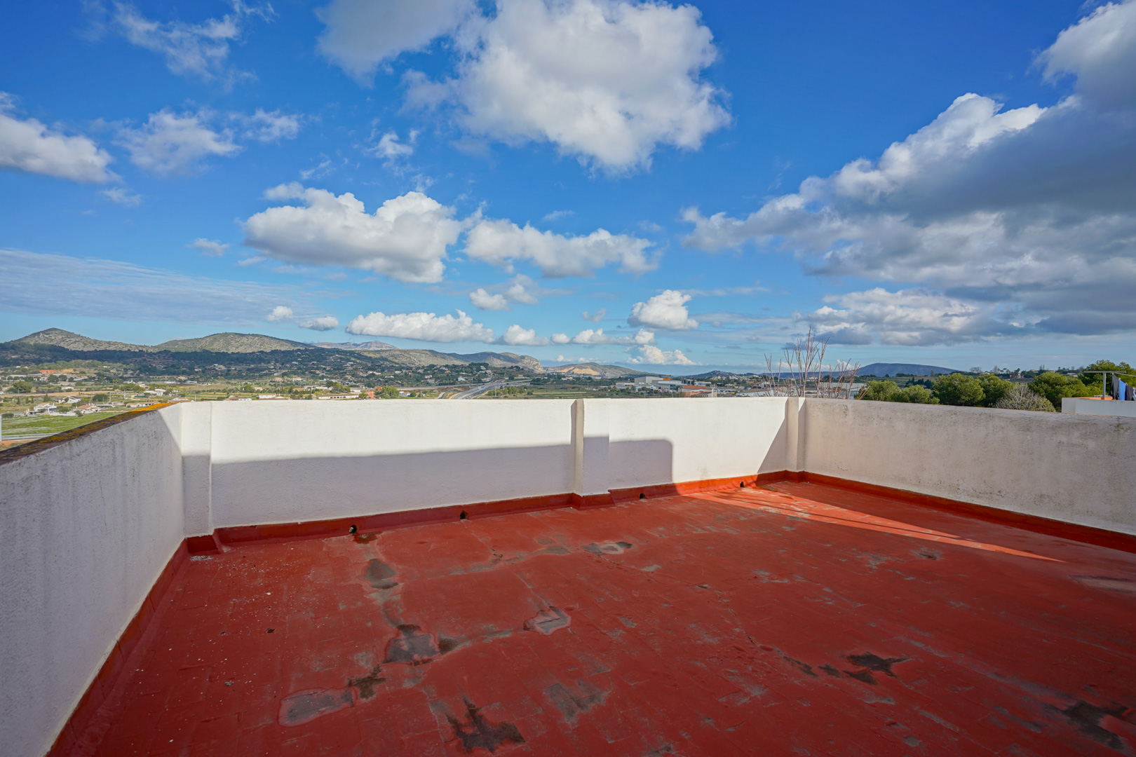 Dakterras met rode vloerafwerking en witte muren, met een panoramisch uitzicht over de bergen en het binnenland van Benissa.