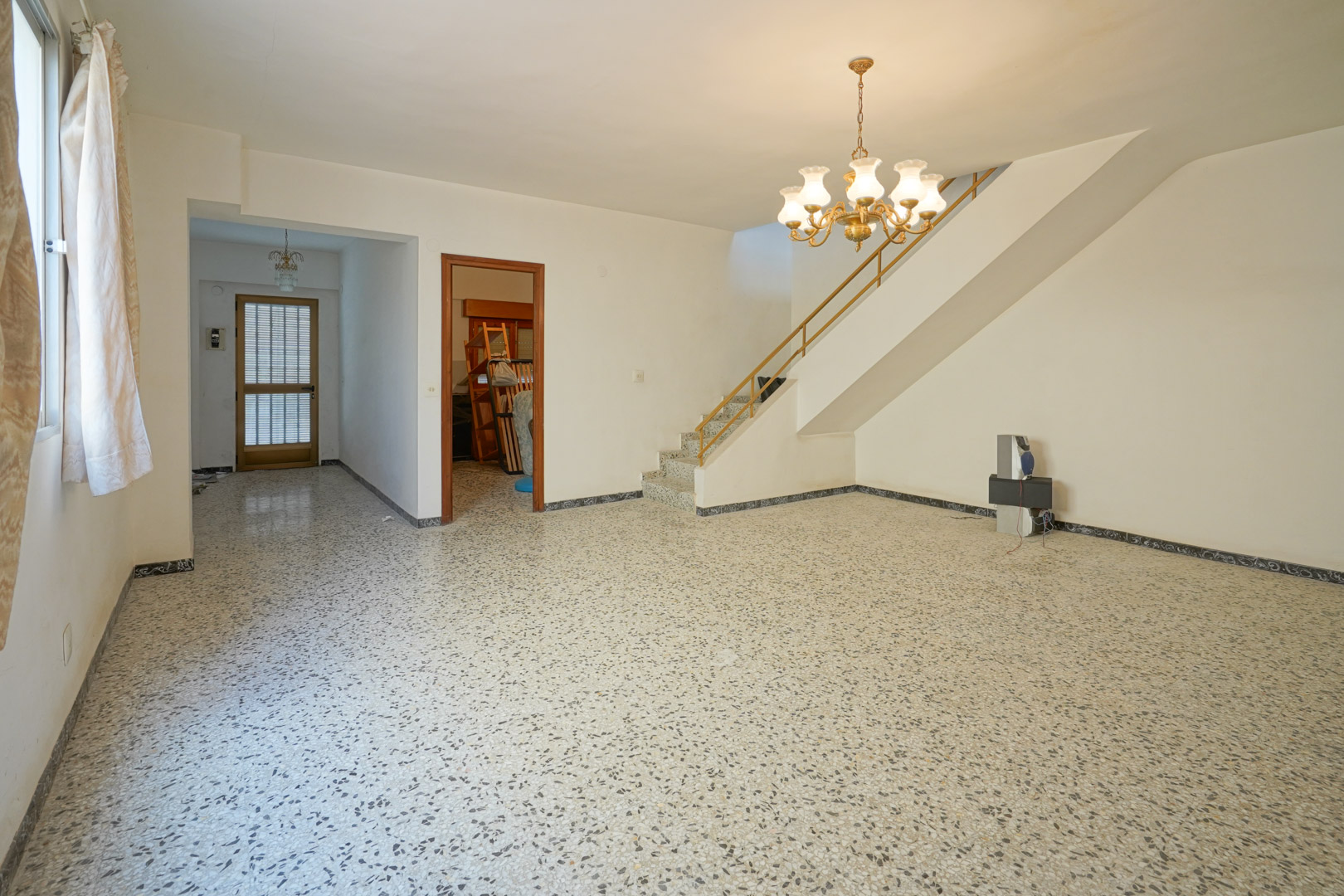 Hoofdwoonkamer met originele terrazzovloer, een vaste trap met metalen leuning en toegang tot de entree en de slaapkamers.