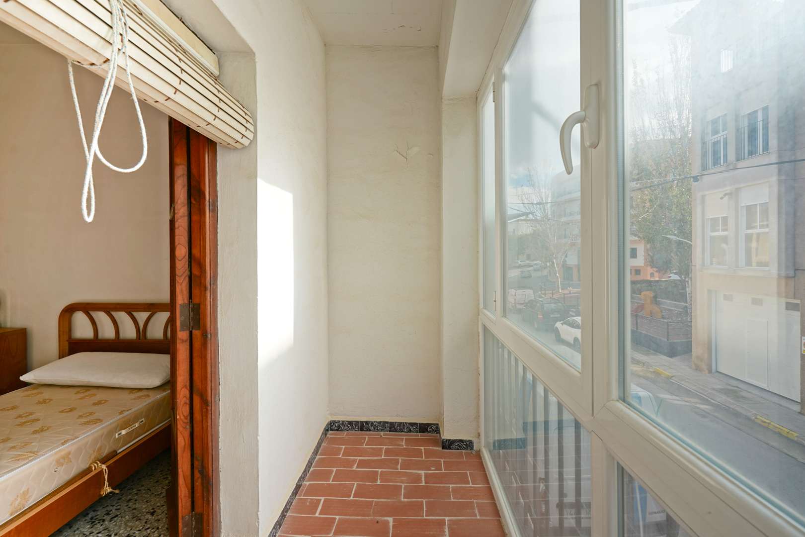 Inpandig balkon met terracotta vloertegels, witte kunststof kozijnen met straatzicht en directe toegang tot een aangrenzende slaapkamer.
