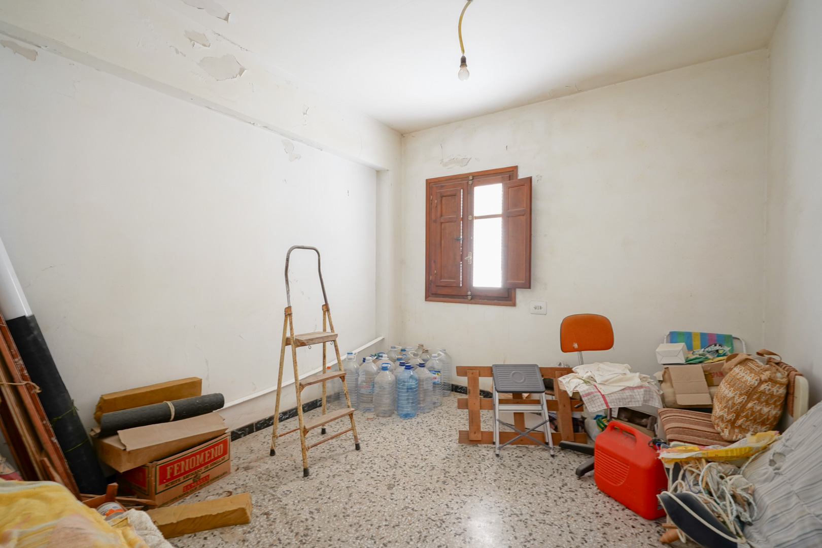 Kamer met terrazzovloer en houten raam met binnenluiken. Deze ruimte toont de noodzaak voor renovatie en het potentieel van de authentieke details.