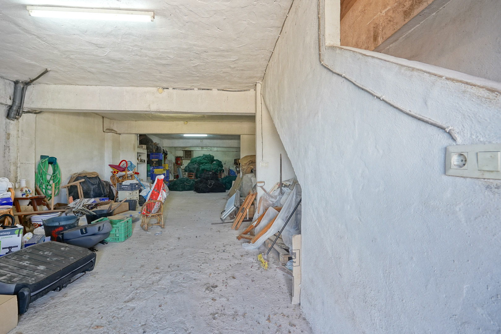 Ruime garage in het souterrain met betonnen vloer en gestuukte wanden. Een zijtrap biedt directe toegang tot de bovengelegen woonverdiepingen.
