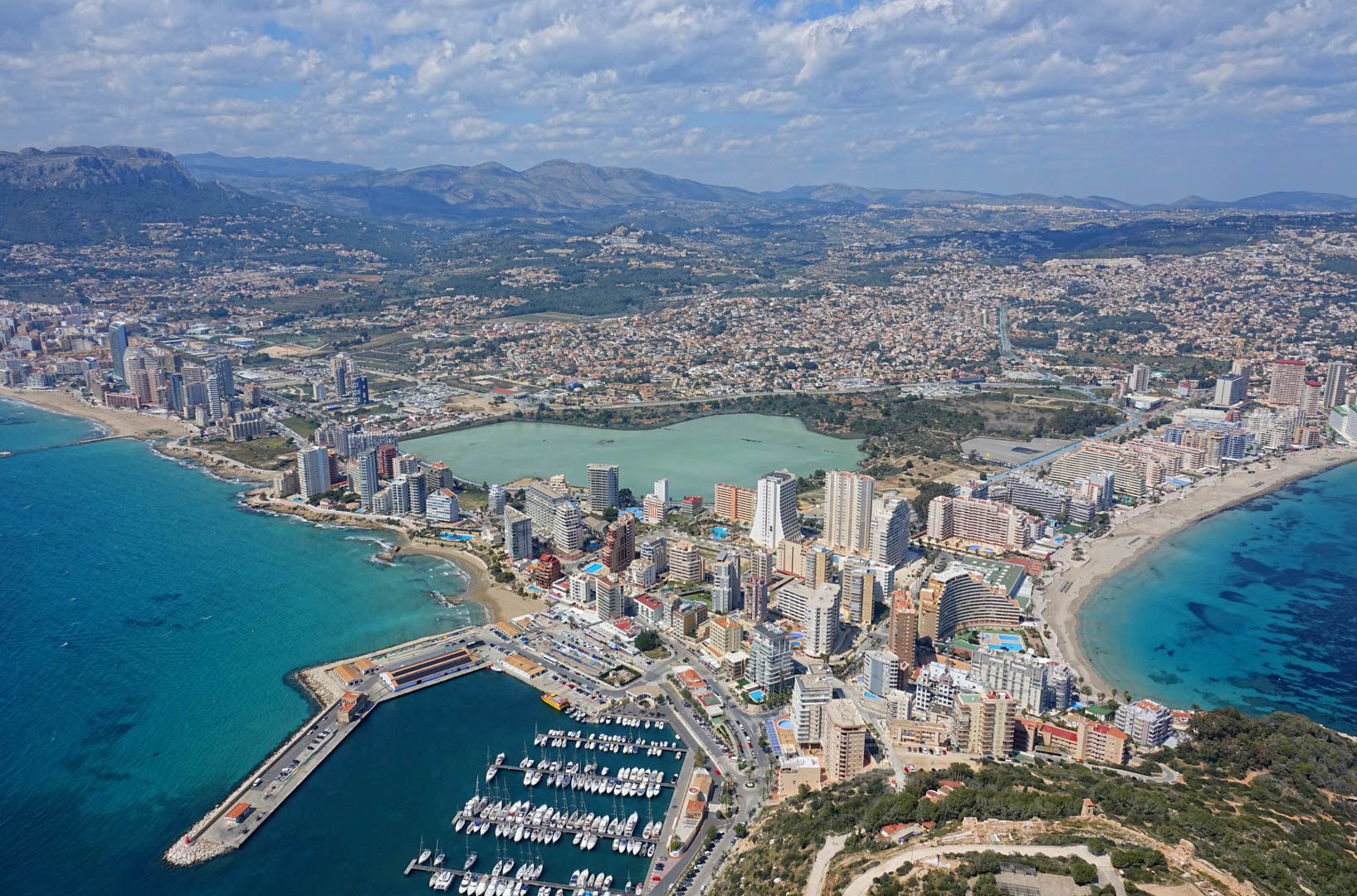 Panoramisch luchtfoto van Calpe met de jachthaven, zandstranden, het zoutmeer Las Salinas en de bergketen Sierra de Bernia op de achtergrond.