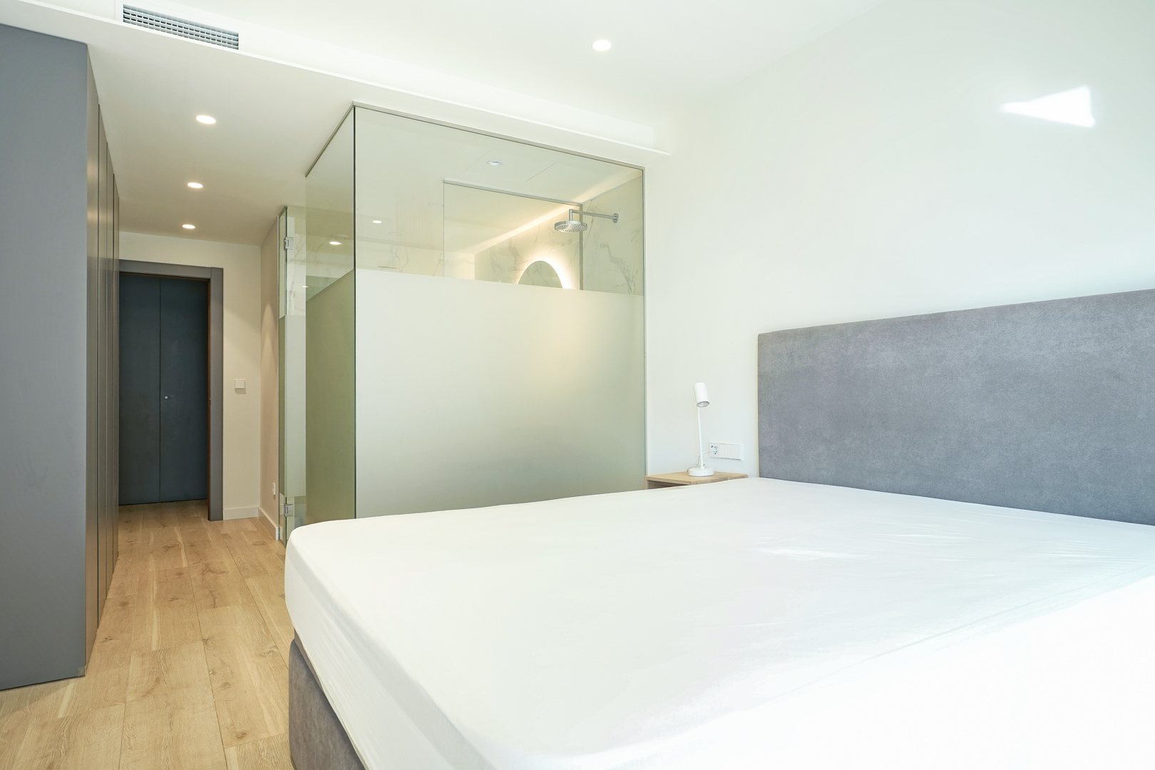 Hoofdslaapkamer met geïntegreerde en-suite badkamer met glazen wanden, inbouwkasten en lichte houten vloer.