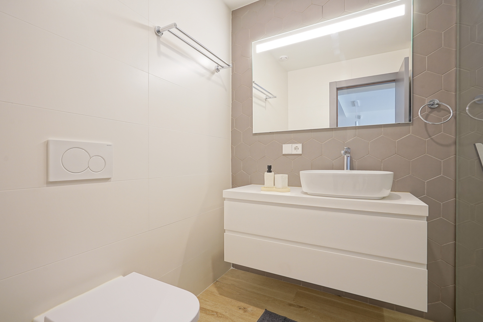 Moderne badkamer met taupekleurige zeshoekige tegels, een wit zwevend wastafelmeubel met opzetkom en een grote spiegel met geïntegreerde ledverlichting.