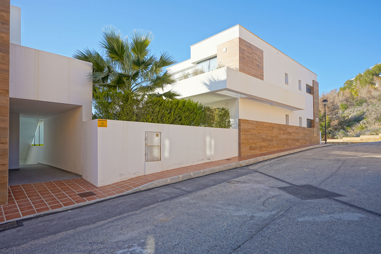 Moderne buitenzijde van het Monte Cala Gardens complex met witte gevels, houtlook accenten en een overdekte toegang tot de woningen.