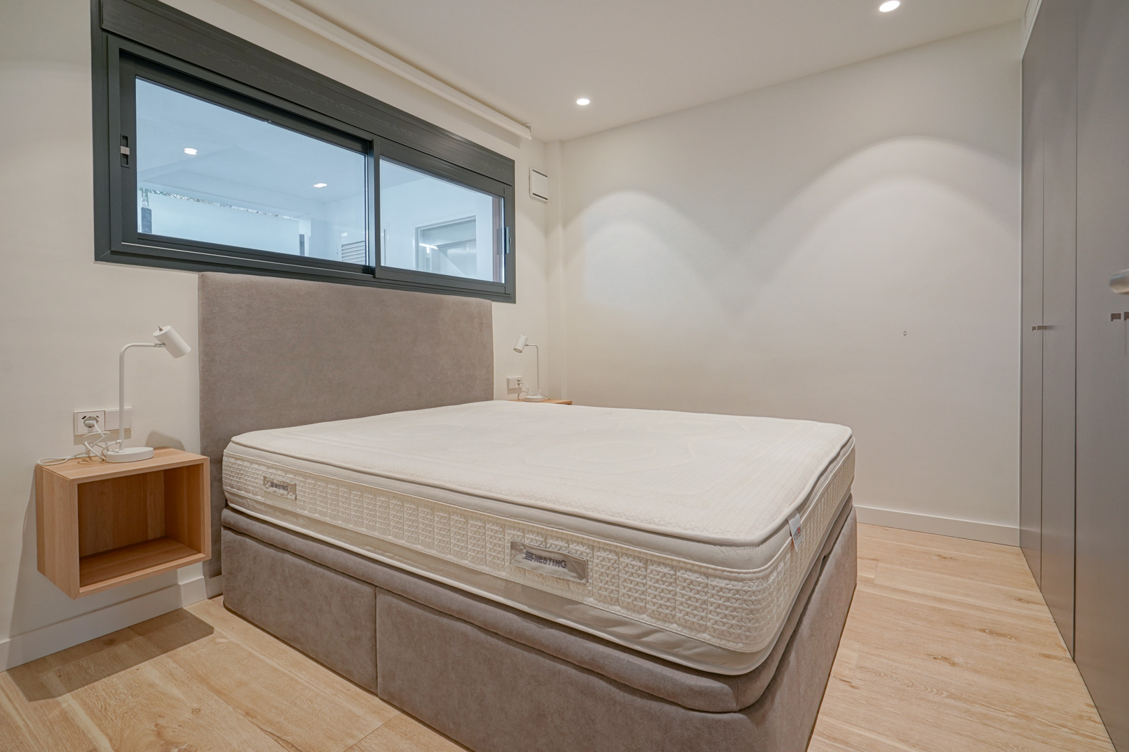 Moderne slaapkamer met tweepersoonsbed, gestoffeerd hoofdbord, inbouwkasten en lichte houten vloer met inbouwspots.