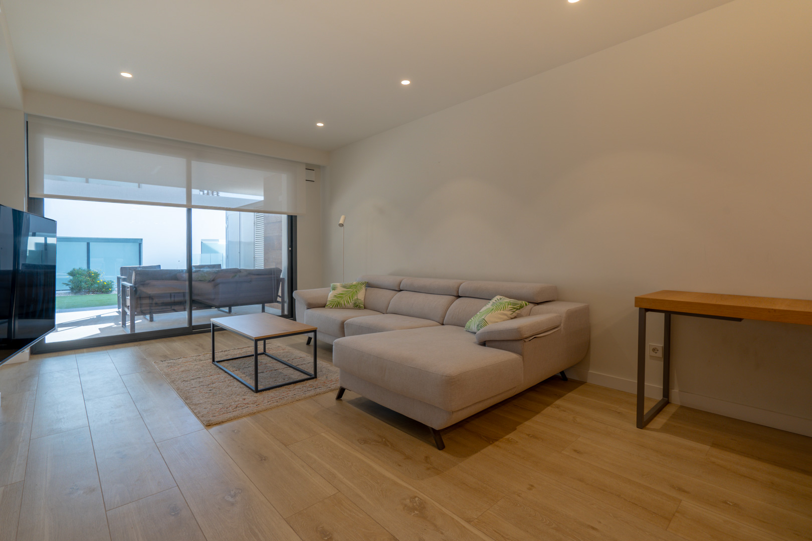 Moderne woonkamer met een grijze chaise longue, lichte houten vloer en grote schuifdeuren die directe toegang bieden tot het terras en de tuin.