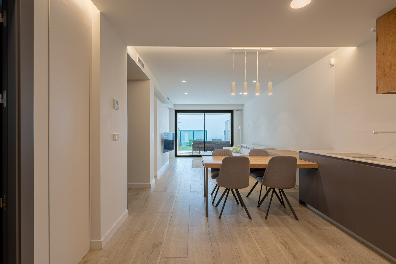 Open woon- en eetkamer met houtlook vloer, indirecte LED-verlichting en grote schuifdeuren die toegang bieden tot het terras en de tuin.