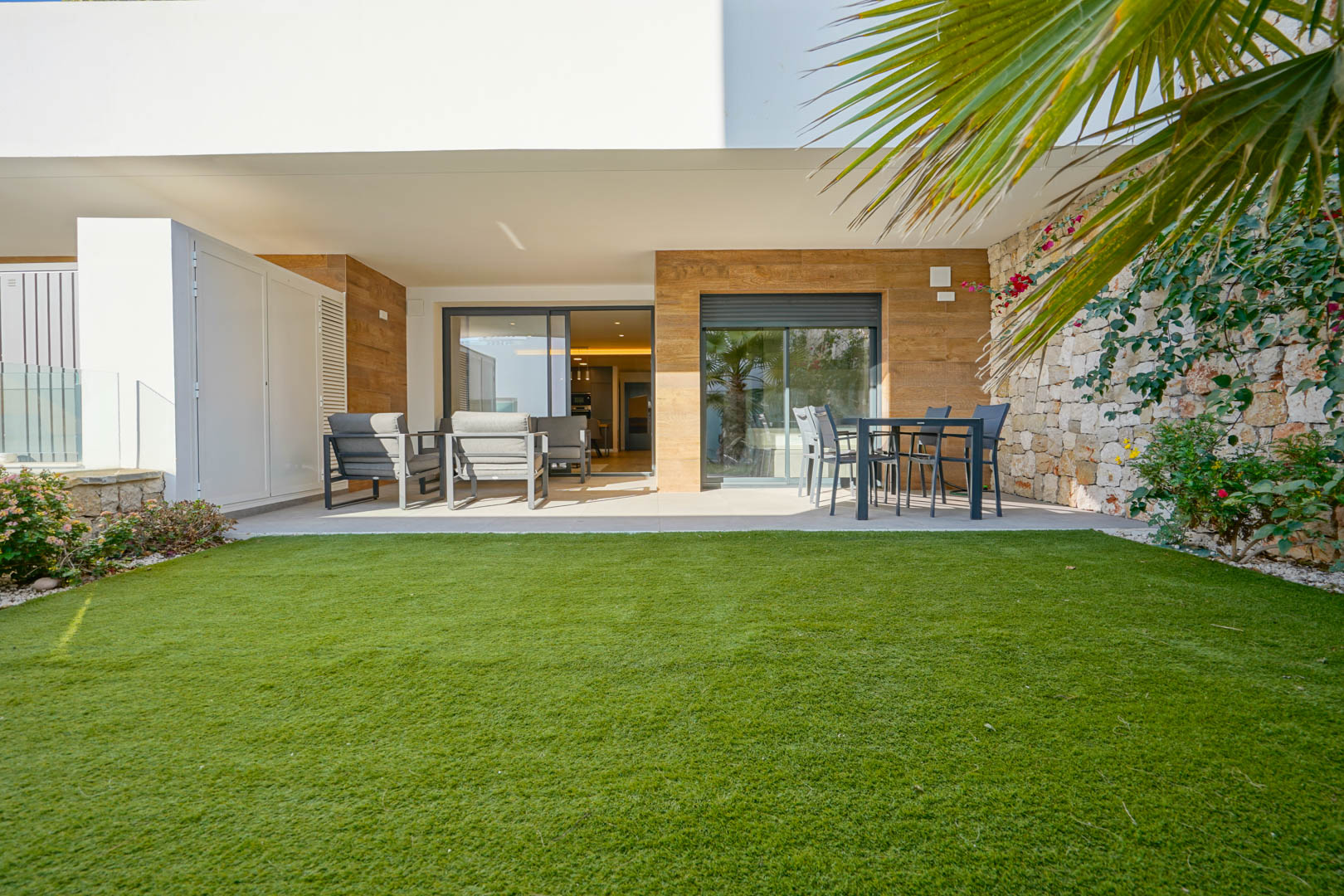 Overdekt terras met loungeset en eethoek, grenzend aan een privétuin met gazon en een karakteristieke natuurstenen muur.