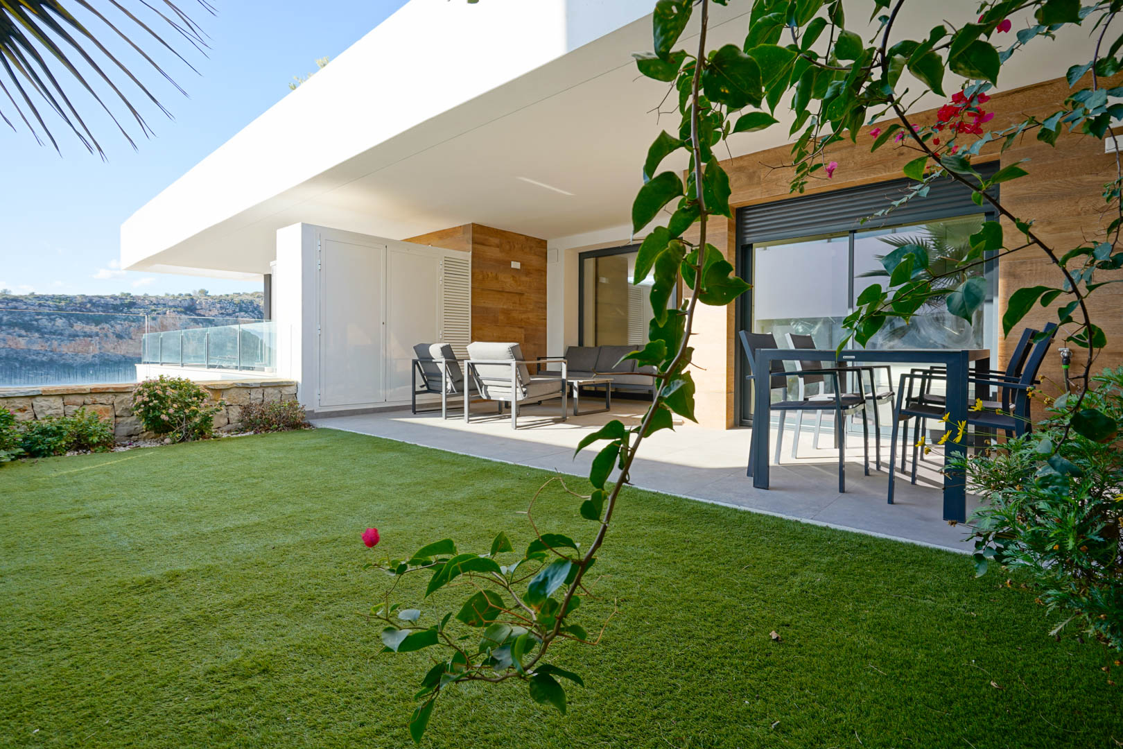 Overdekt terras met modern tuinmeubilair en een privétuin met kunstgras, omheind door een natuurstenen muur met uitzicht op het natuurpark.