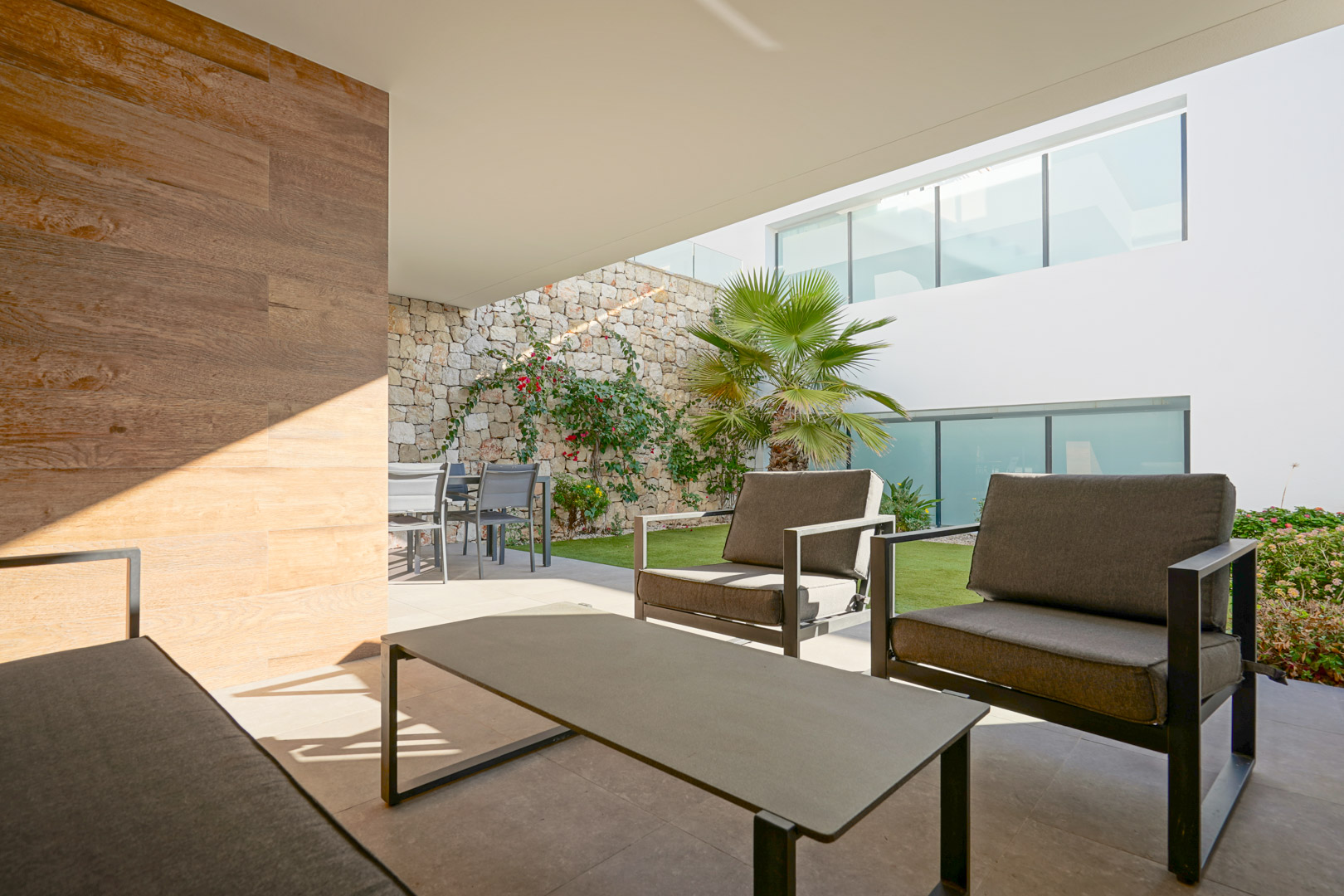 Overdekt terras met moderne zithoek, eethoek en privétuin met natuurstenen muur en mediterrane beplanting.