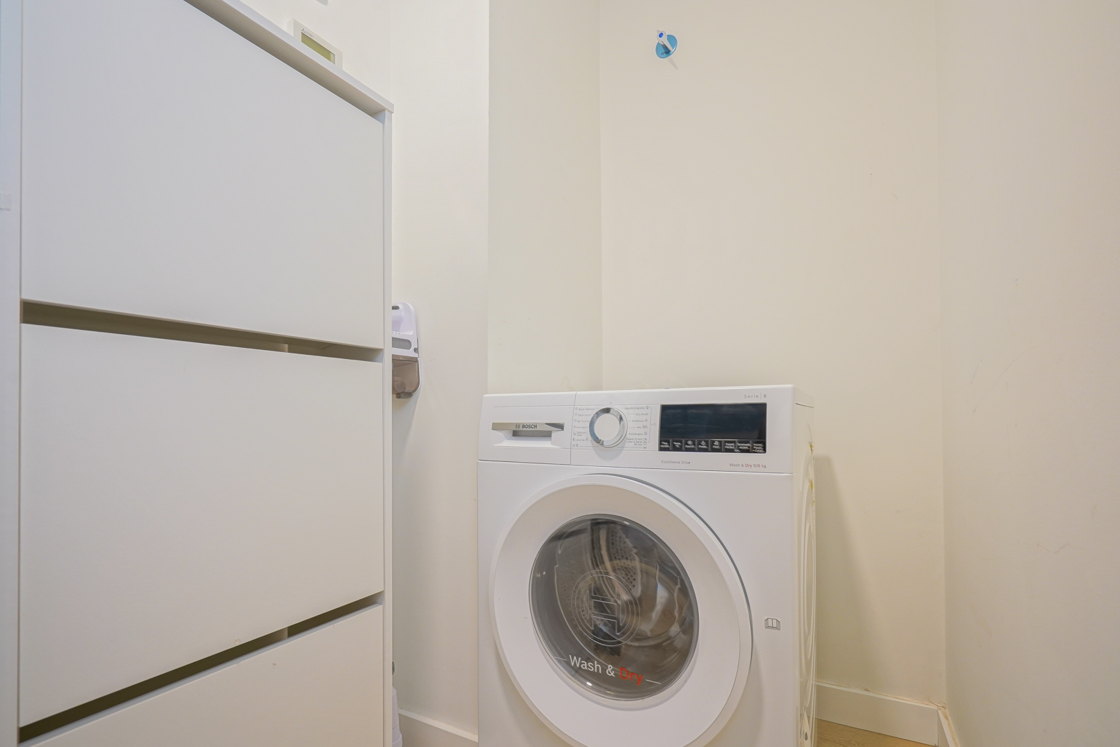 Praktische wasruimte uitgerust met een Bosch was-droogcombinatie en een witte opbergkast, gelegen direct naast de entree.