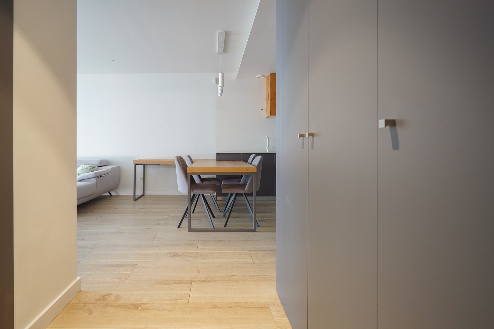 Zicht vanuit de hal met grijze inbouwkasten, lichte houten vloeren en een open eethoek met houten tafel en moderne hanglamp.