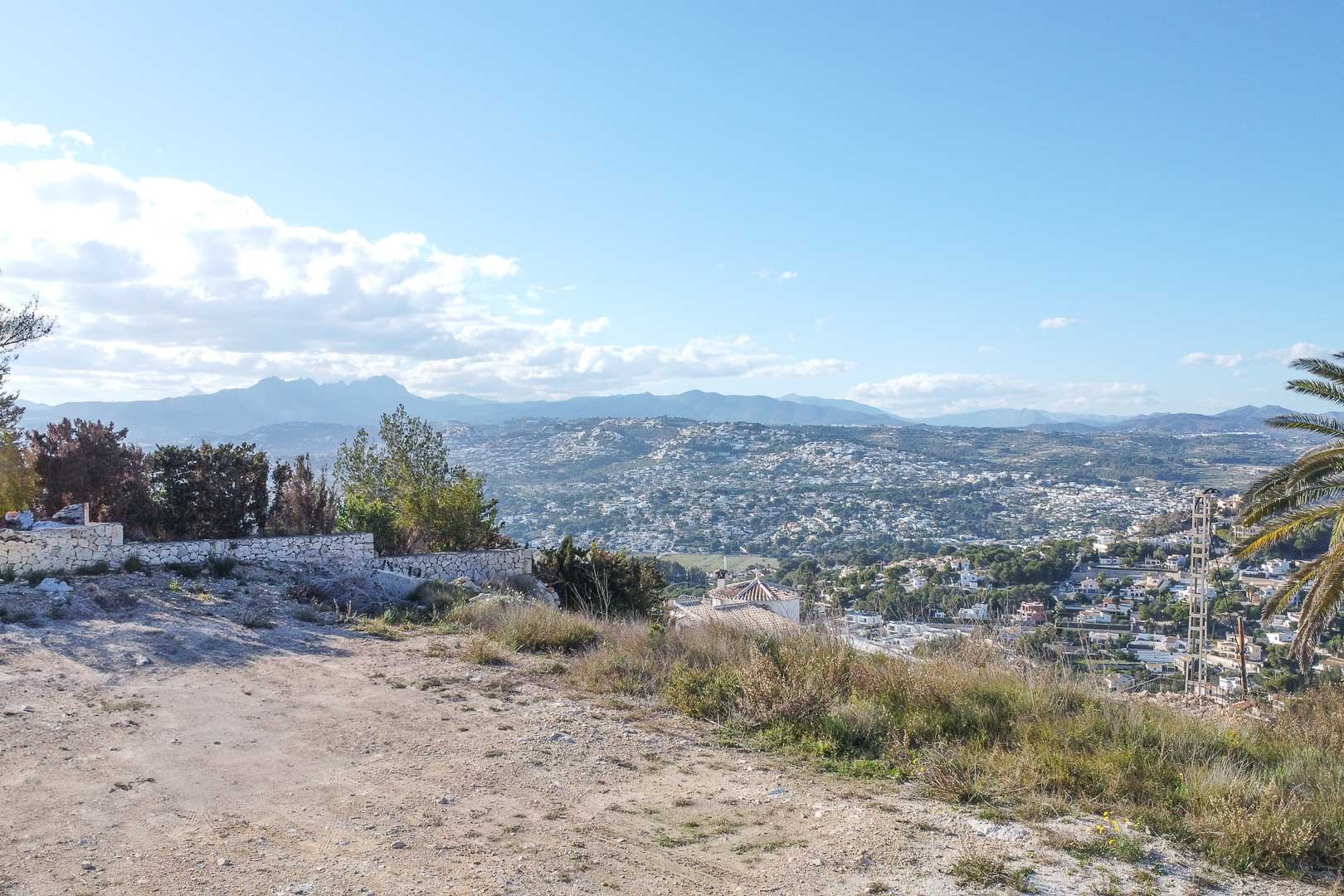 Panoramisch uitzicht op Moraira vanaf verhoogd terrein met stenen muur en vegetatie.
