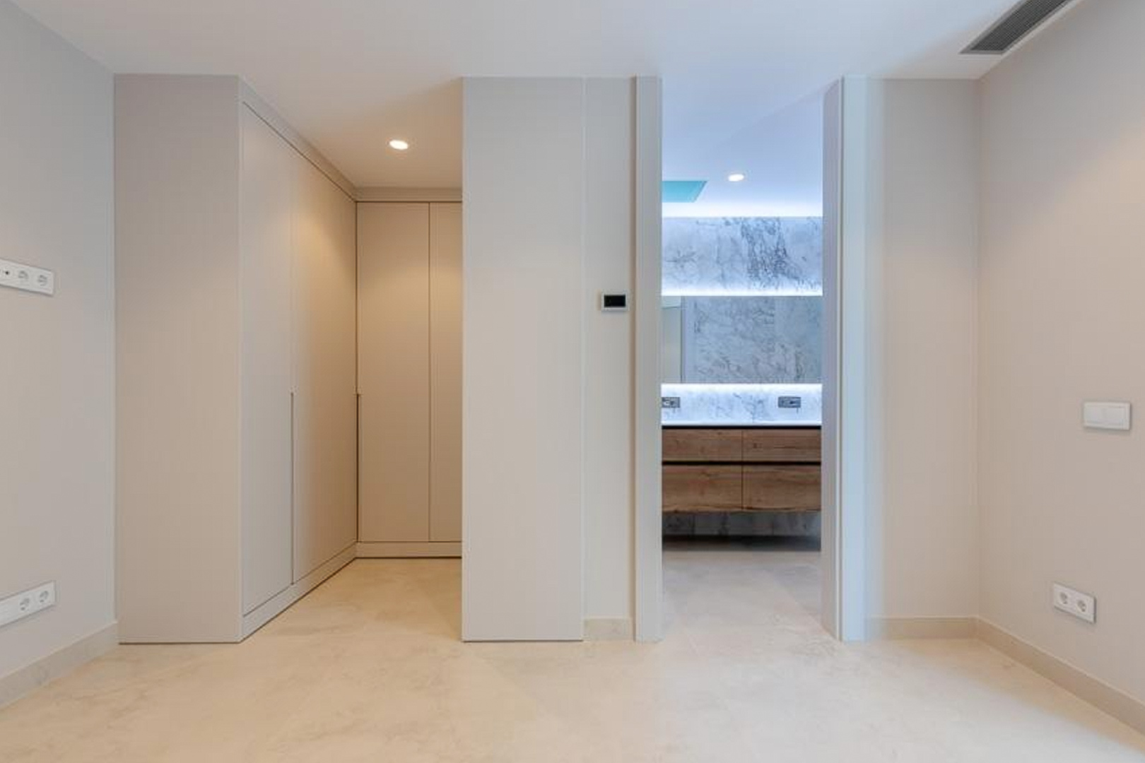 Hoofdslaapkamer met kamerhoge inbouwkasten en een en-suite badkamer voorzien van marmeren wanden, een houten wastafelmeubel en indirecte led-verlichting.
