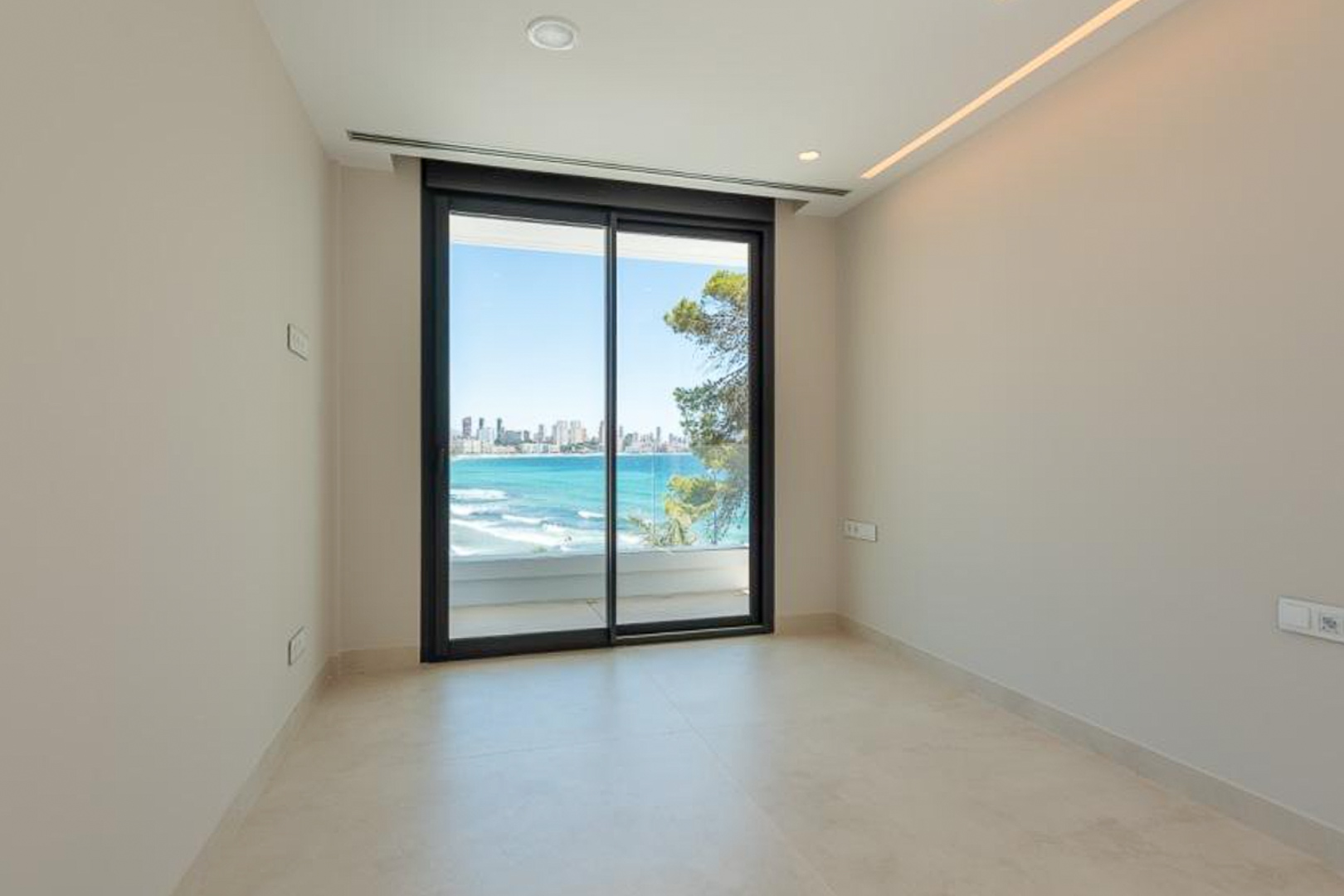 Lichte kamer met porseleinen vloertegels, geïntegreerde LED-verlichting en schuifpui naar het terras met panoramisch uitzicht op zee en Benidorm.