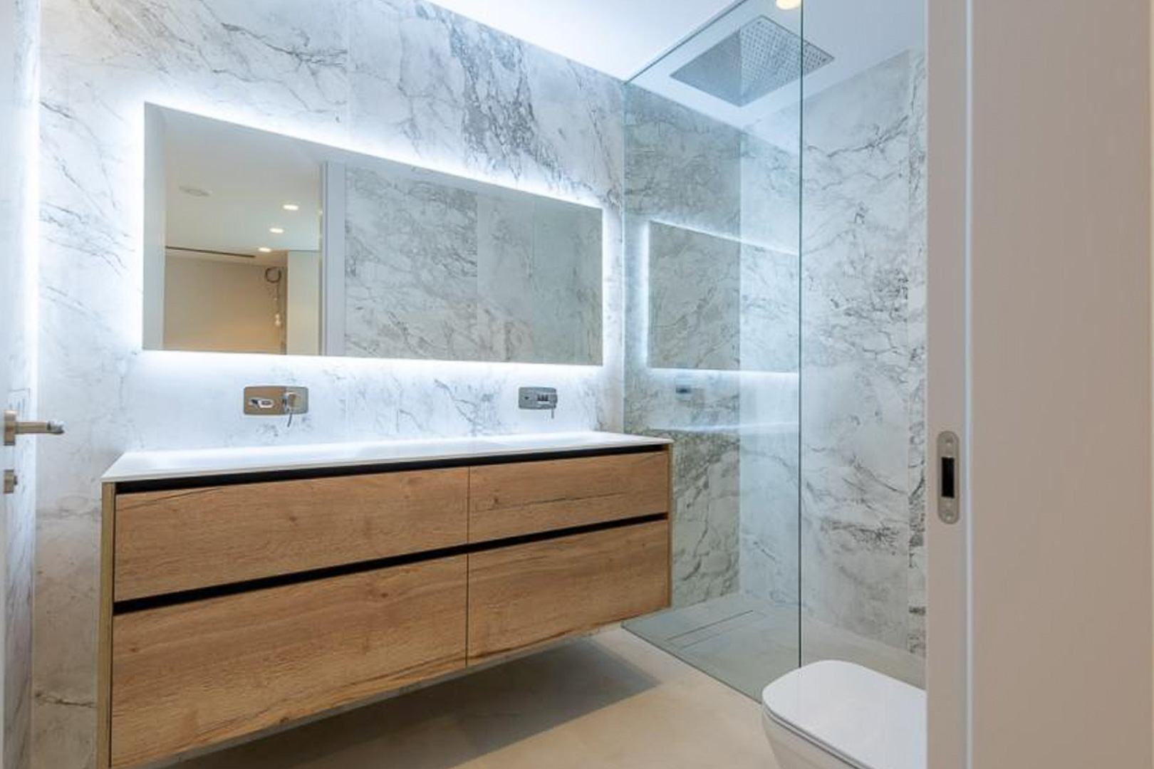 Moderne badkamer met marmerlook tegels, zwevend houten dubbel wastafelmeubel en een verlichte spiegel. Inclusief inloopdouche met glazen wand.