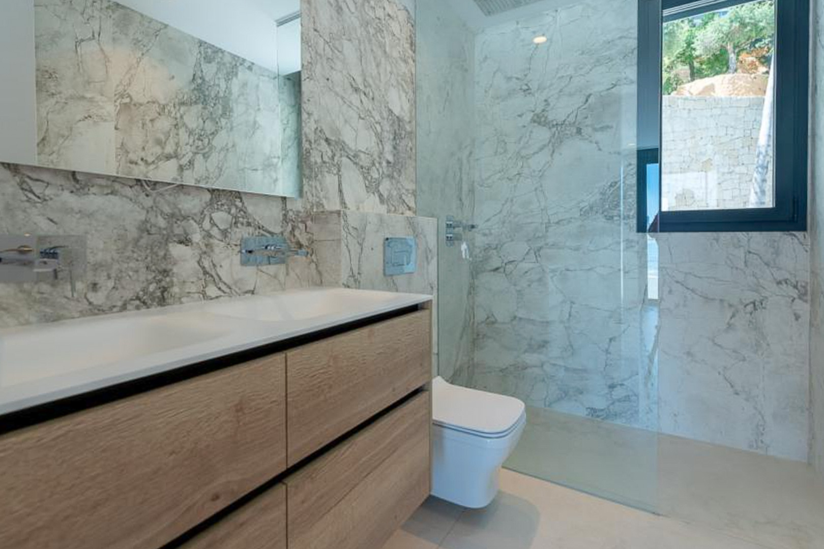 Moderne badkamer met marmerlook wandtegels, een dubbel wastafelmeubel in licht hout en een inloopdouche met glazen wand.