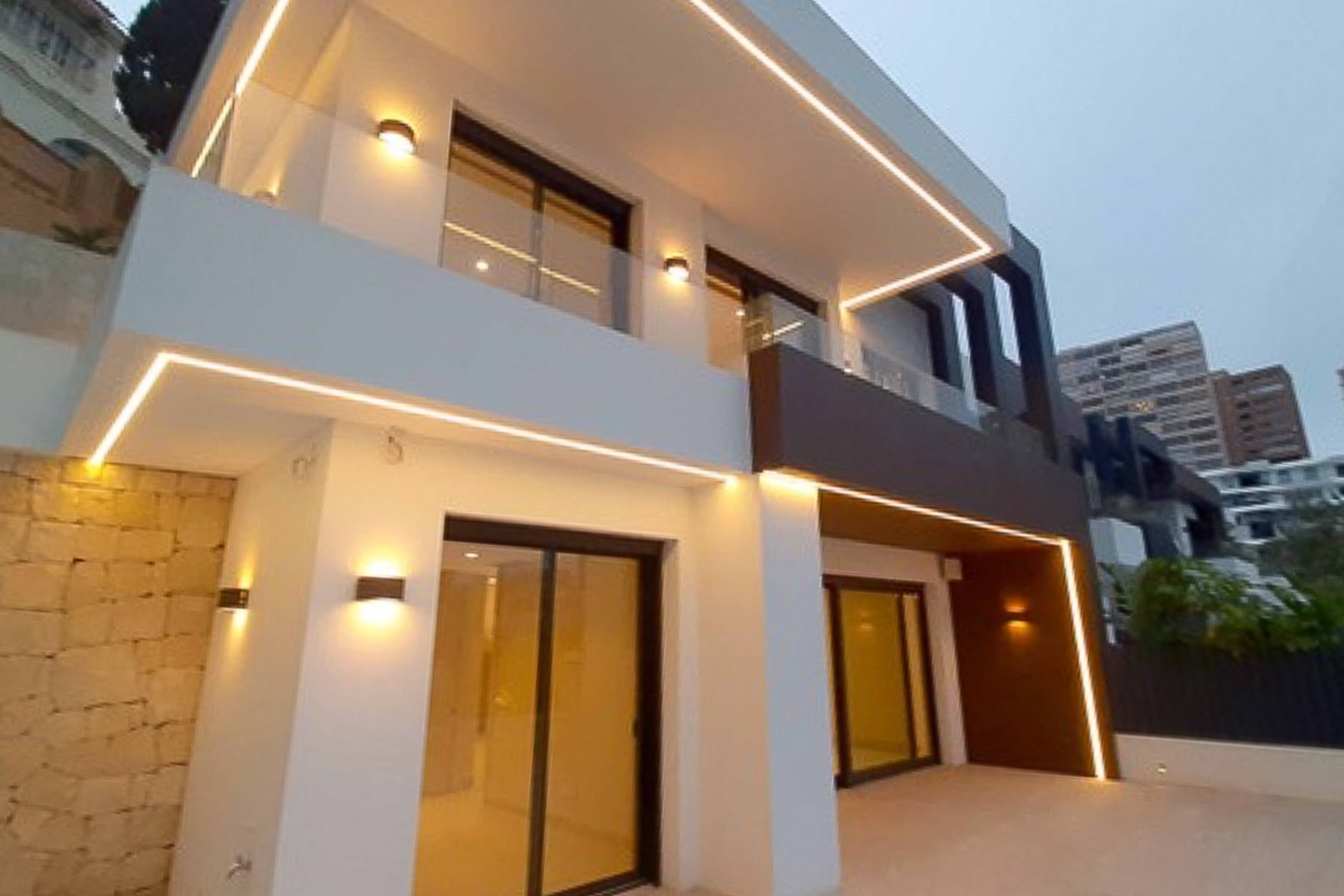 Moderne buitengevel met geïntegreerde LED-verlichting, glazen balustrades en grote glazen schuifdeuren in een minimalistische stijl.