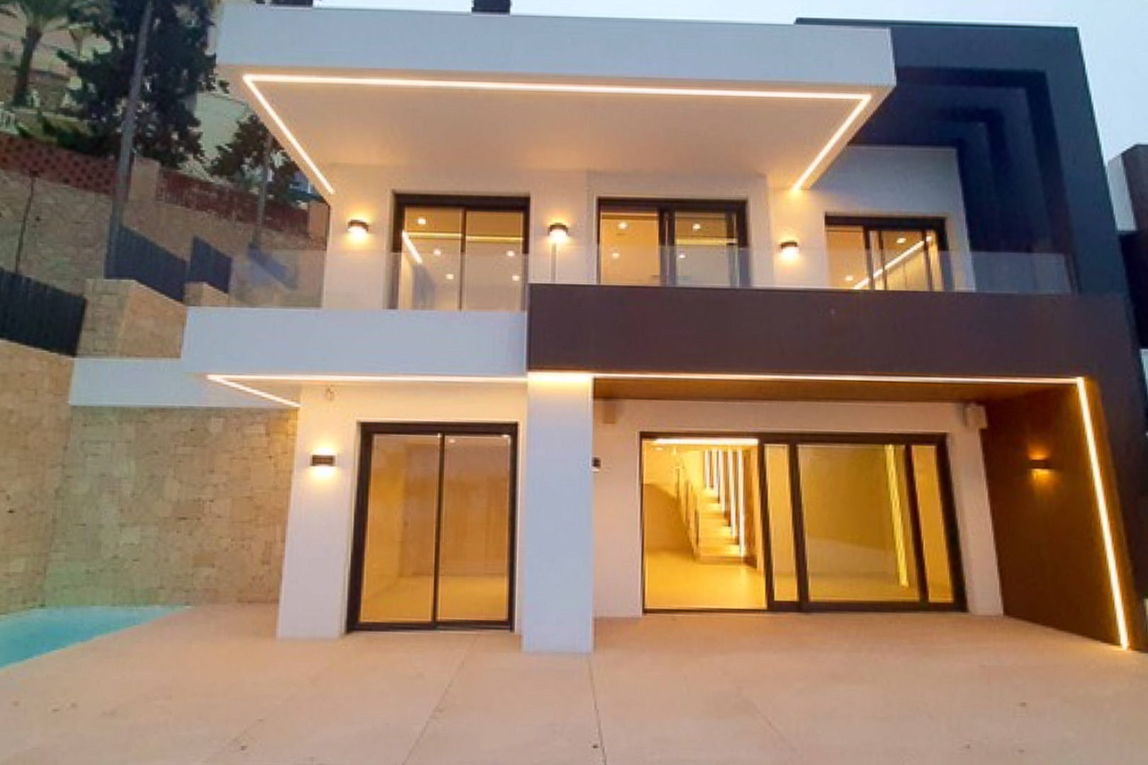 Moderne gevel met geïntegreerde LED-verlichting, grote glazen schuifdeuren en terrassen met glazen balustrades in een ontwerp van contrasterende volumes.