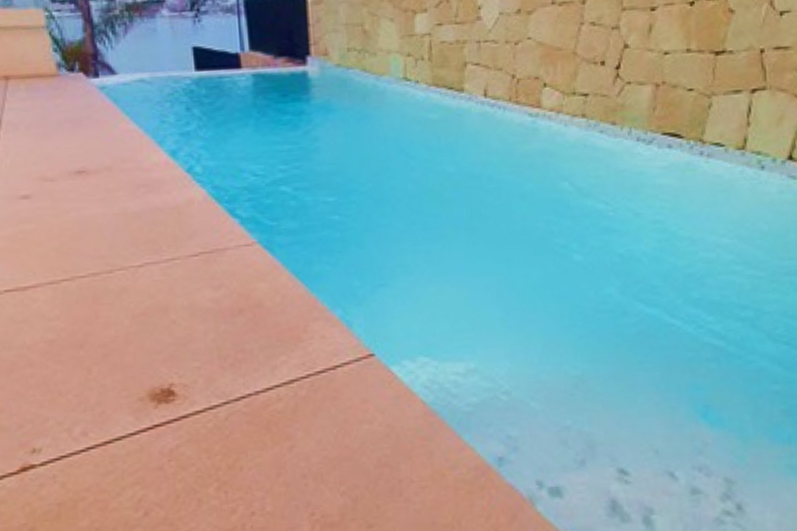 Privé overloopzwembad met uitzicht op zee, afgewerkt met een terras in terracotta-tinten en een wand van natuursteen.