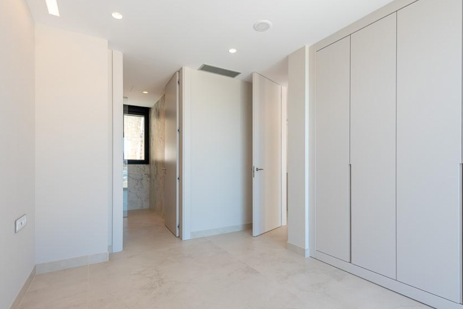 Slaapkamer met kamerhoge inbouwkasten, geïntegreerde plafondverlichting en toegang tot een en-suite badkamer met marmeren wandafwerking.