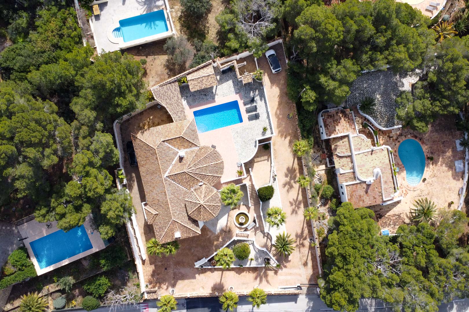Bovenaanzicht van de villa met terracotta pannendaken, een rechthoekig zwembad en stenen terrassen, omgeven door een volgroeide mediterrane tuin.