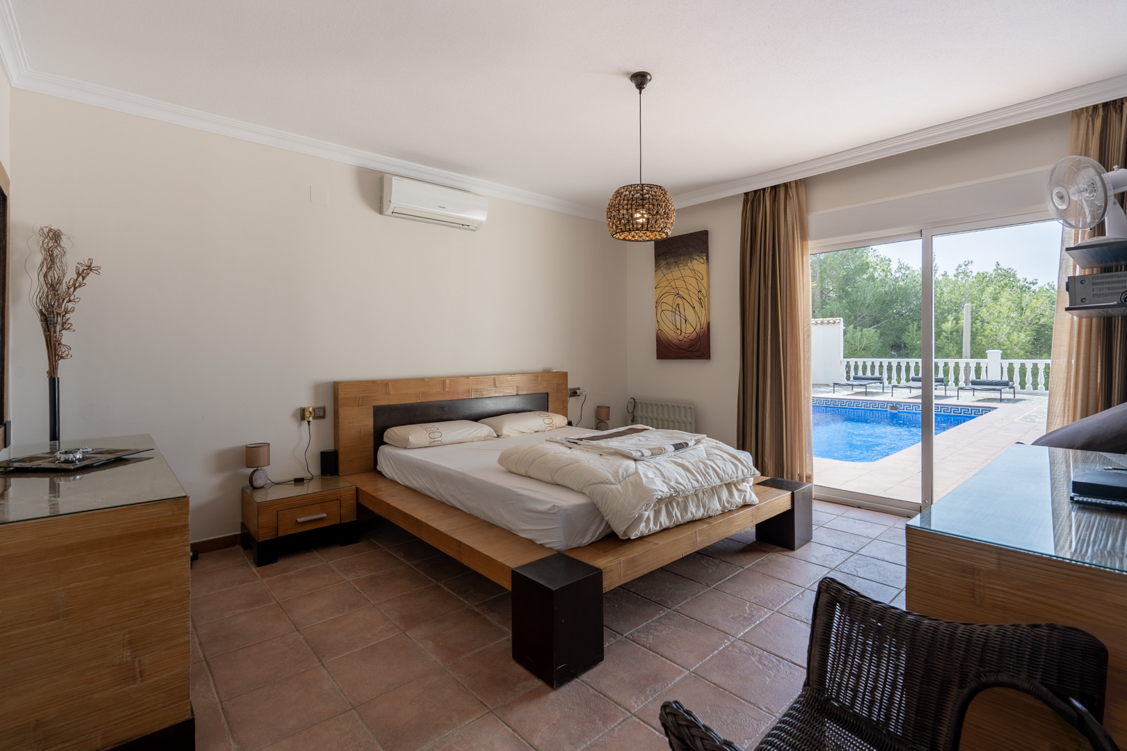 Hoofdslaapkamer met terracotta vloer, airconditioning en directe toegang tot het zwembadterras via grote glazen schuifdeuren.