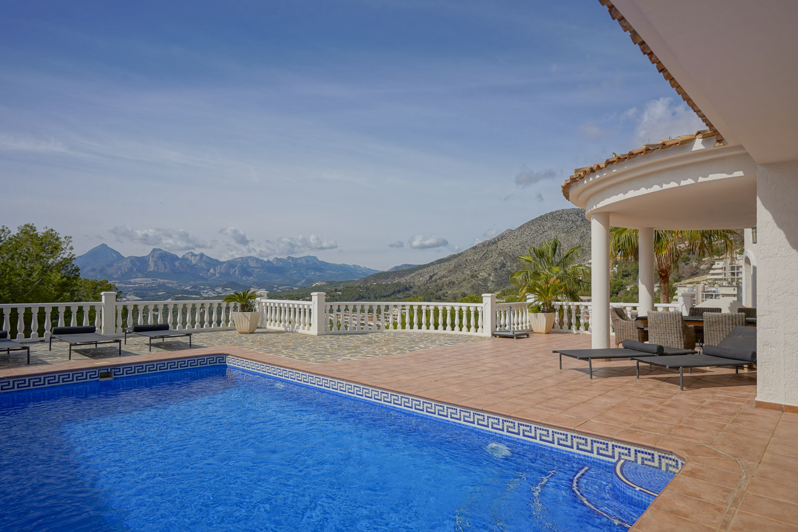 Hoofdterras met blauw betegeld zwembad, ligstoelen en een overdekte veranda. Het biedt een panoramisch uitzicht op de bergen Puig Campana en Sierra Aitana.
