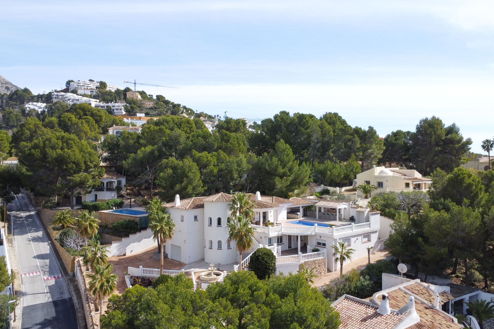 Luchtfoto van de mediterrane villa met witte gevel, ronde toren en zwembadterras, omgeven door een weelderig pijnbomenbos in Altea.