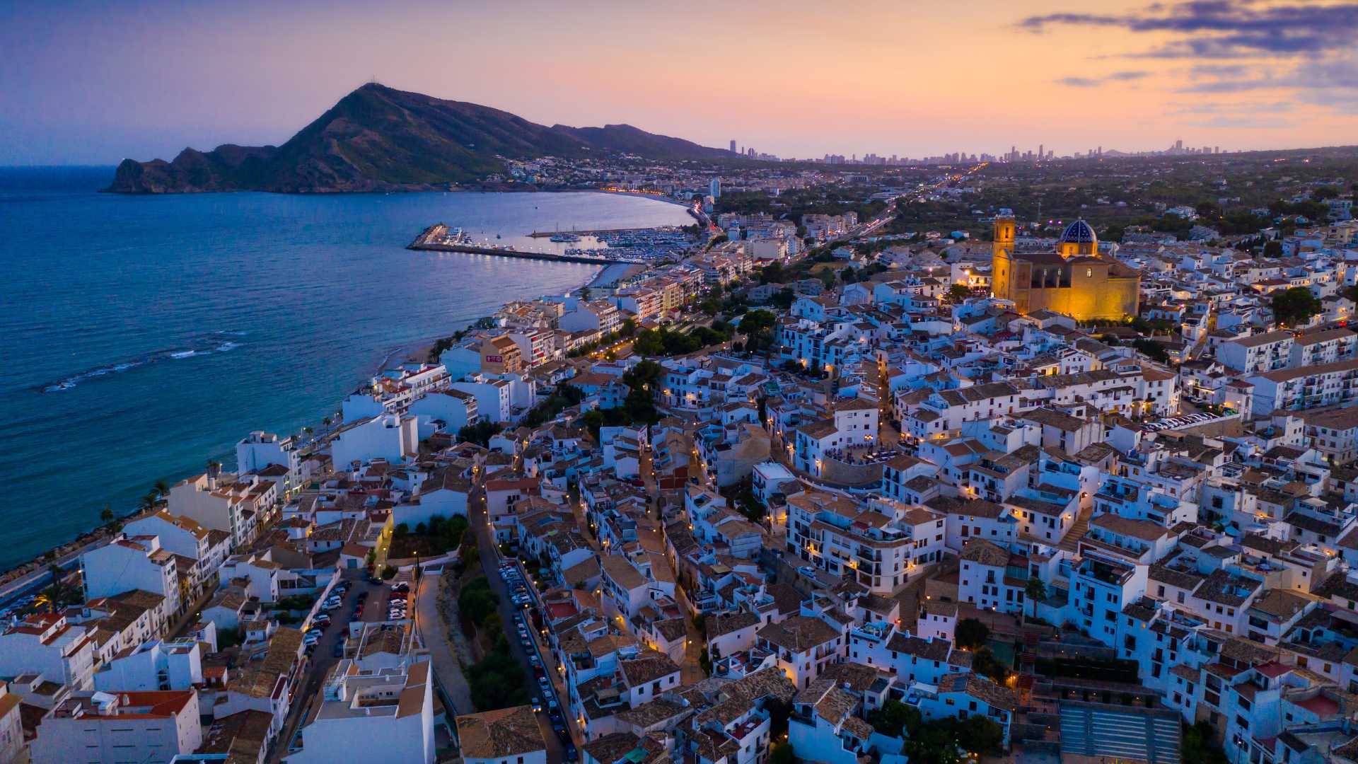 Luchtfoto van het oude centrum van Altea bij schemering, met de iconische kerk met blauwe koepel, witgekalkte huizen en een panoramisch uitzicht over de kustlijn.