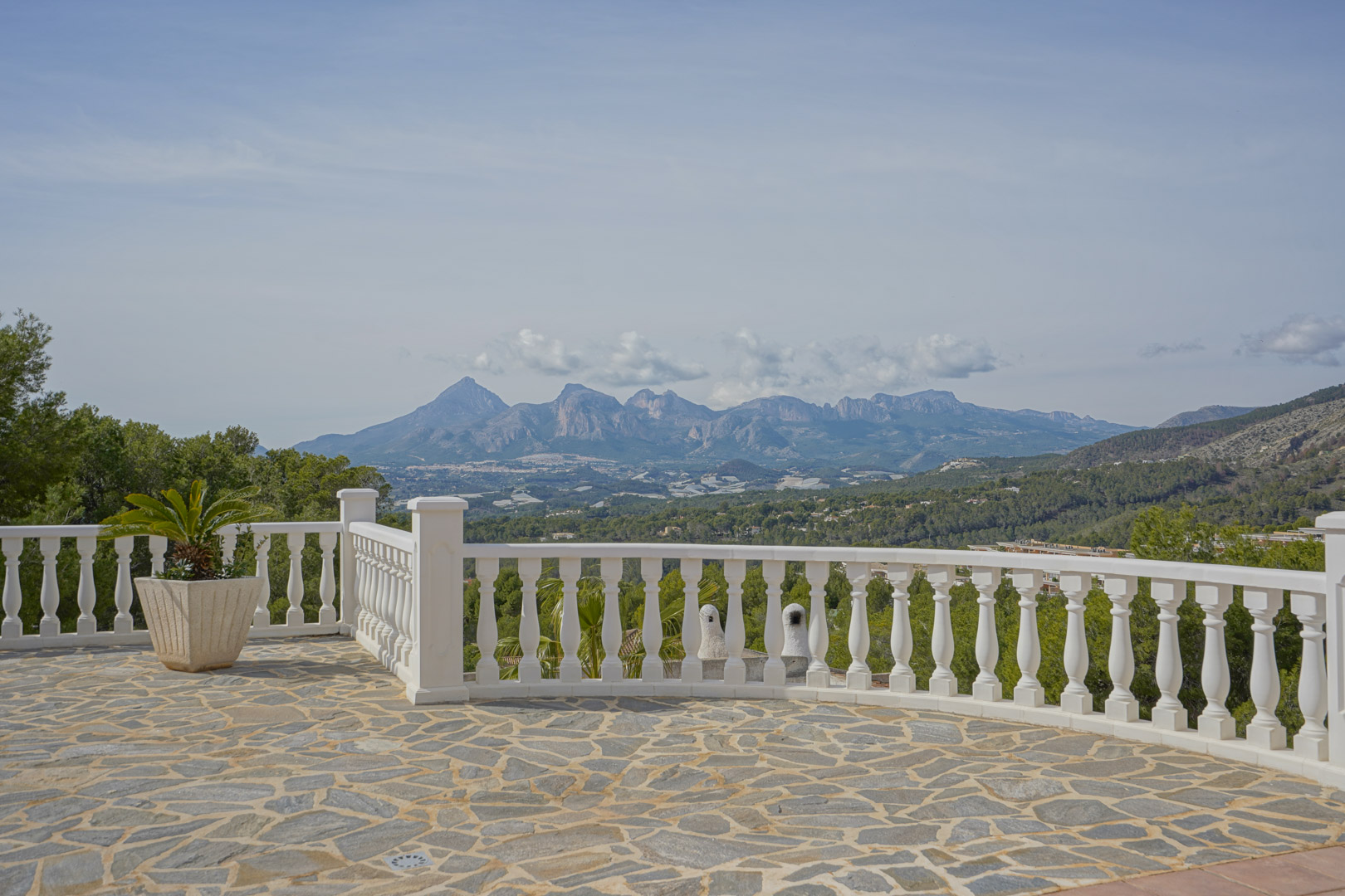 Met natuursteen geplaveid terras met een witte balustrade en panoramisch uitzicht op de bergketens Puig Campana en Sierra Aitana.