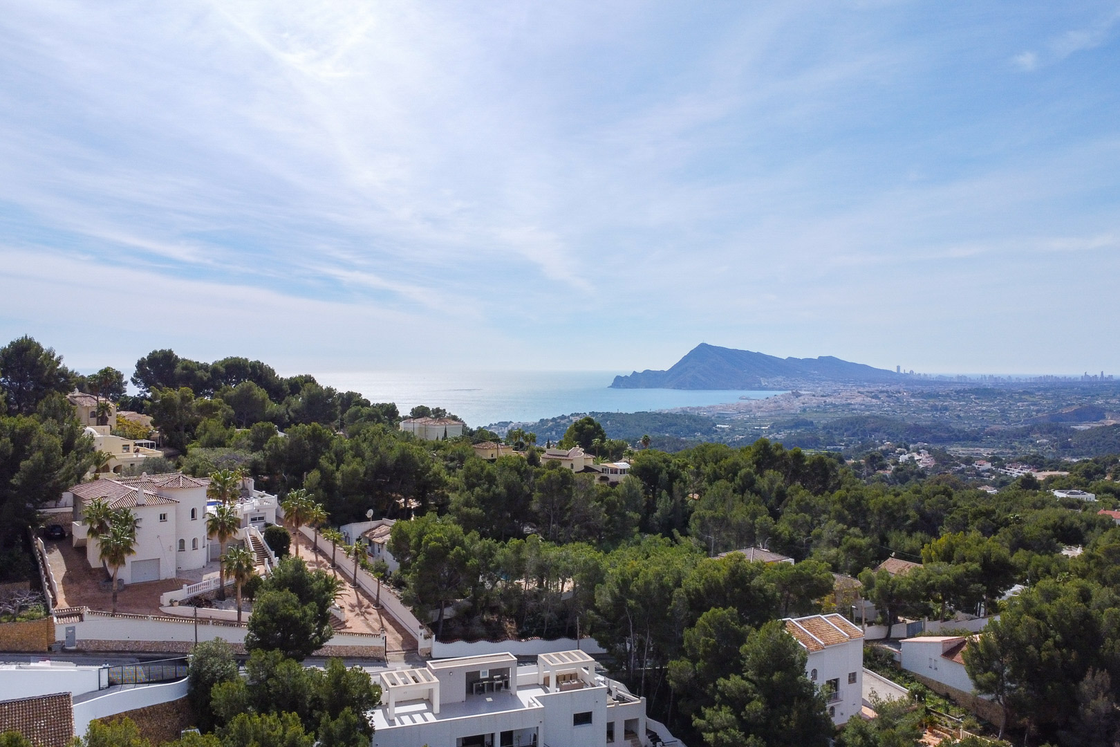Panoramisch luchtaanzicht van de bosrijke omgeving met witte villa's en de kustlijn die reikt tot aan de skyline van Benidorm in de verte.