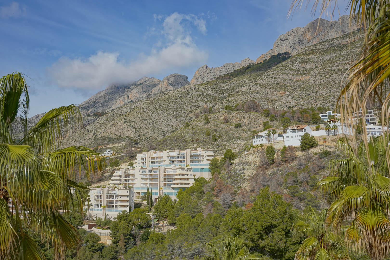 Panoramisch uitzicht op het Sierra de Bernia-gebergte, met de karakteristieke rotstoppen en woonwijken die tegen de beboste helling zijn gebouwd.