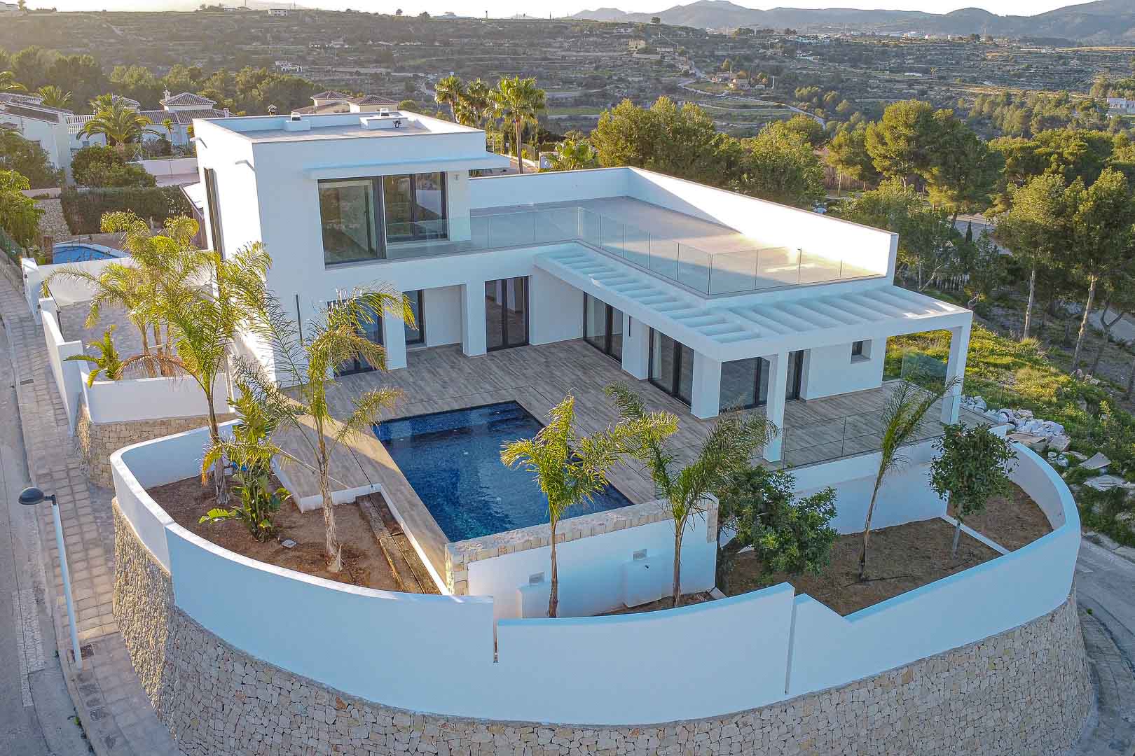 Luchtfoto van moderne villa met blauw zwembad en witte muren met stenen details in Benimeit, Moraira.