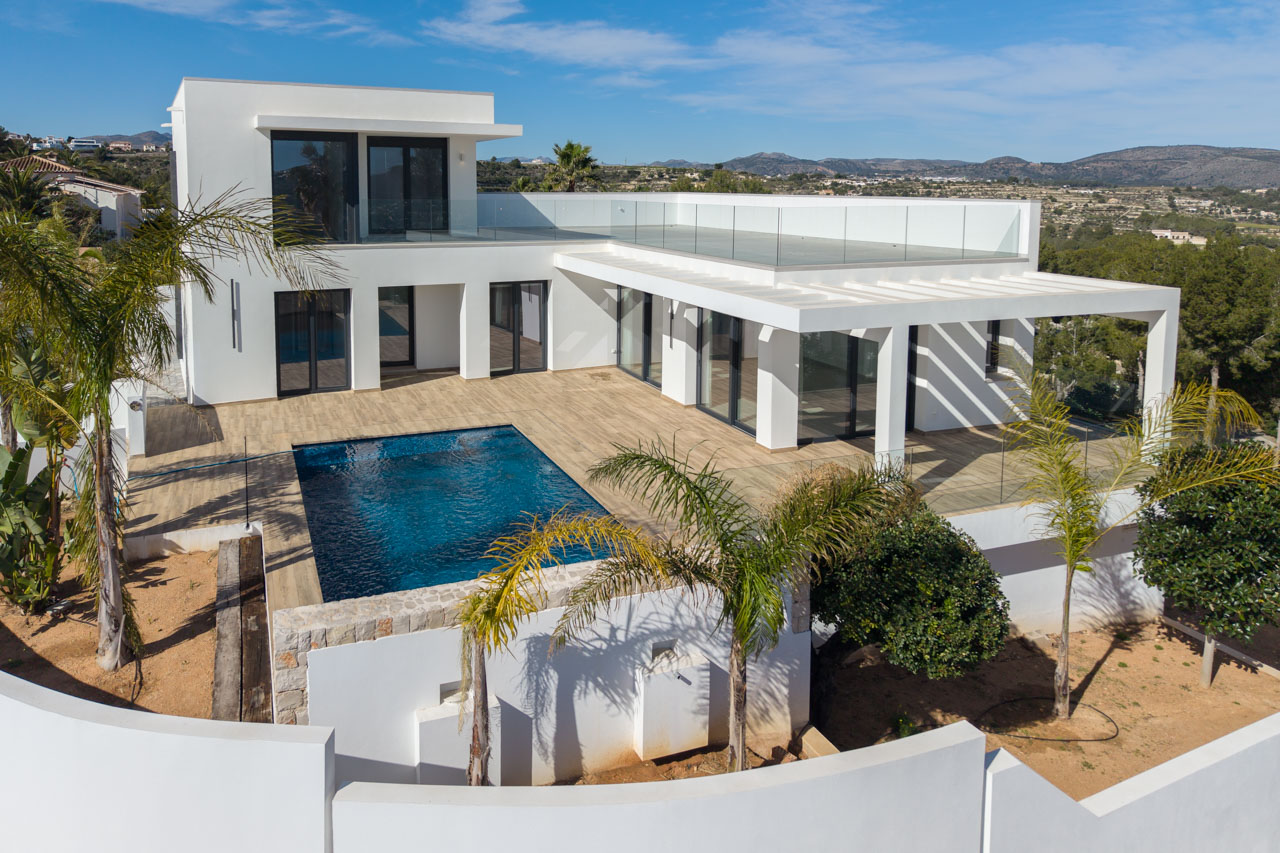 Luchtfoto van moderne villa met blauw zwembad, houten terras en glazen balustrade in Benimeit, Moraira.