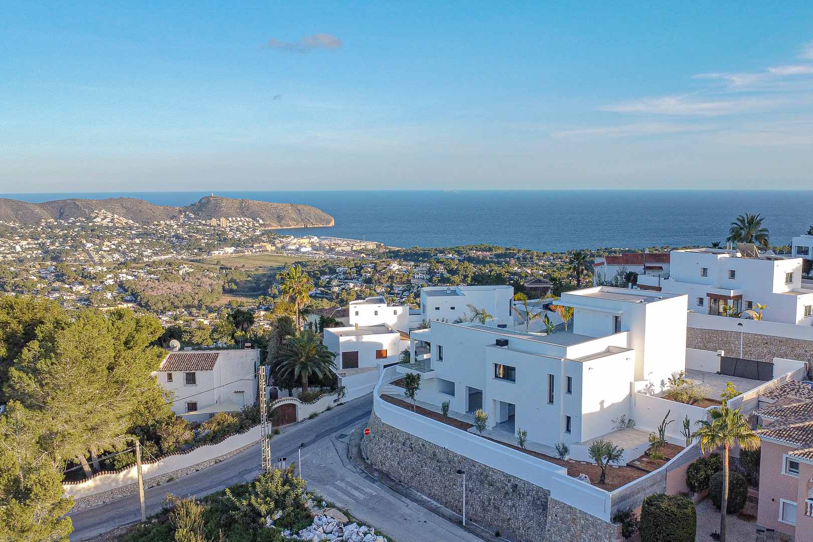 Verhoogd uitzicht op moderne witte villa's in Benimeit met panoramisch uitzicht op de zee en de kustlijn.