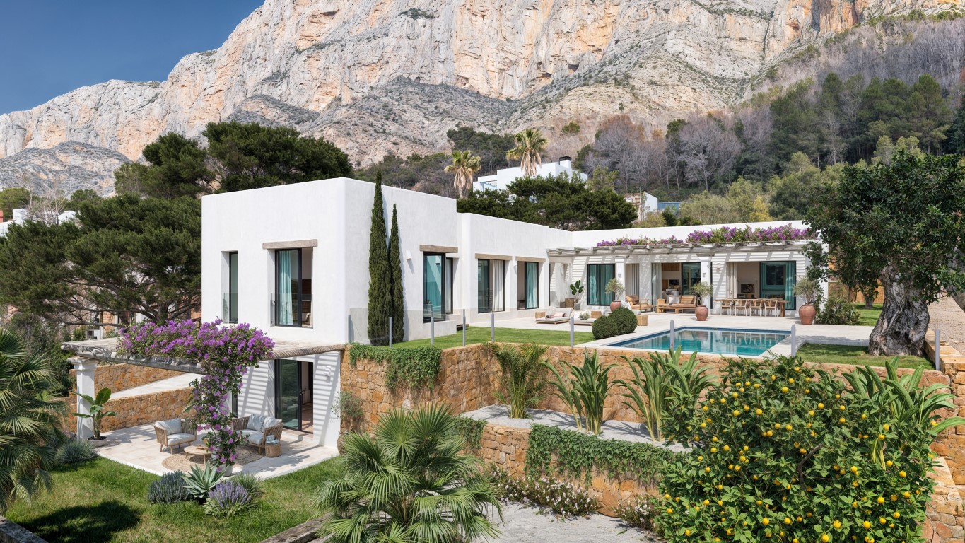Exterieur van de villa met witte gevels, privézwembad en natuurstenen muren, gelegen tegen de indrukwekkende rotswanden van de Montgó in Jávea.