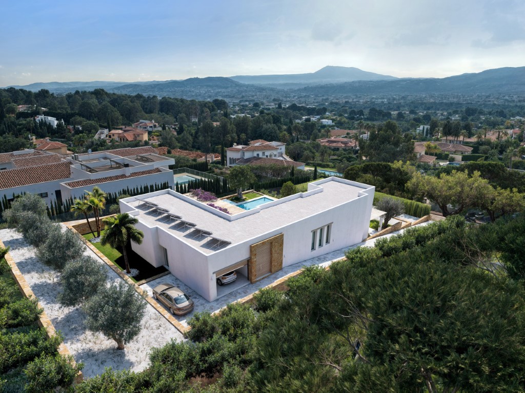 Luchtfoto van de moderne L-vormige villa met zonnepanelen, inpandige garage en een aangelegde tuin met weids uitzicht over de vallei.